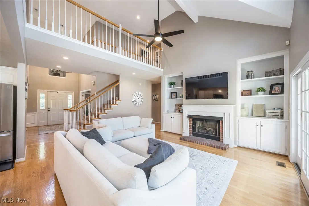 Living room featuring high vaulted ceiling, ceiling fan, light hardwood floors, beam ceiling, and a brick gas fireplace