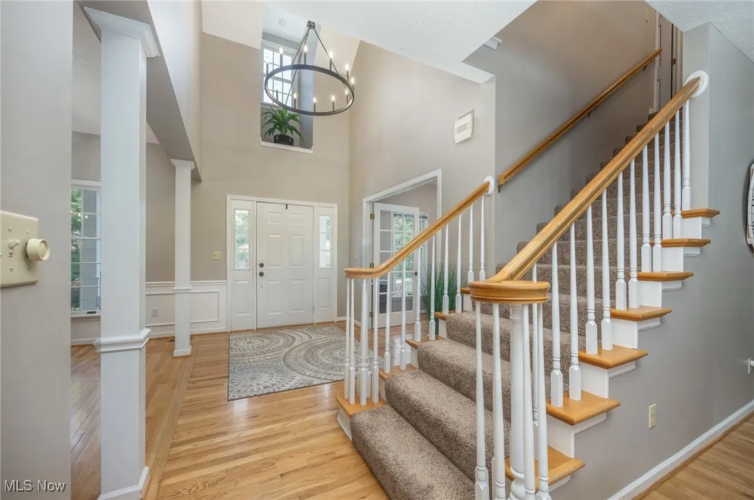Foyer entrance featuring wood finished floors, decorative columns, a chandelier, stairs, and a high ceiling