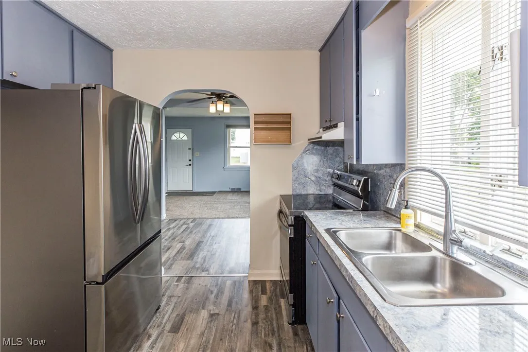 Kitchen with stainless steel appliances, arched walkways, dark wood finished floors, backsplash, and ceiling fan