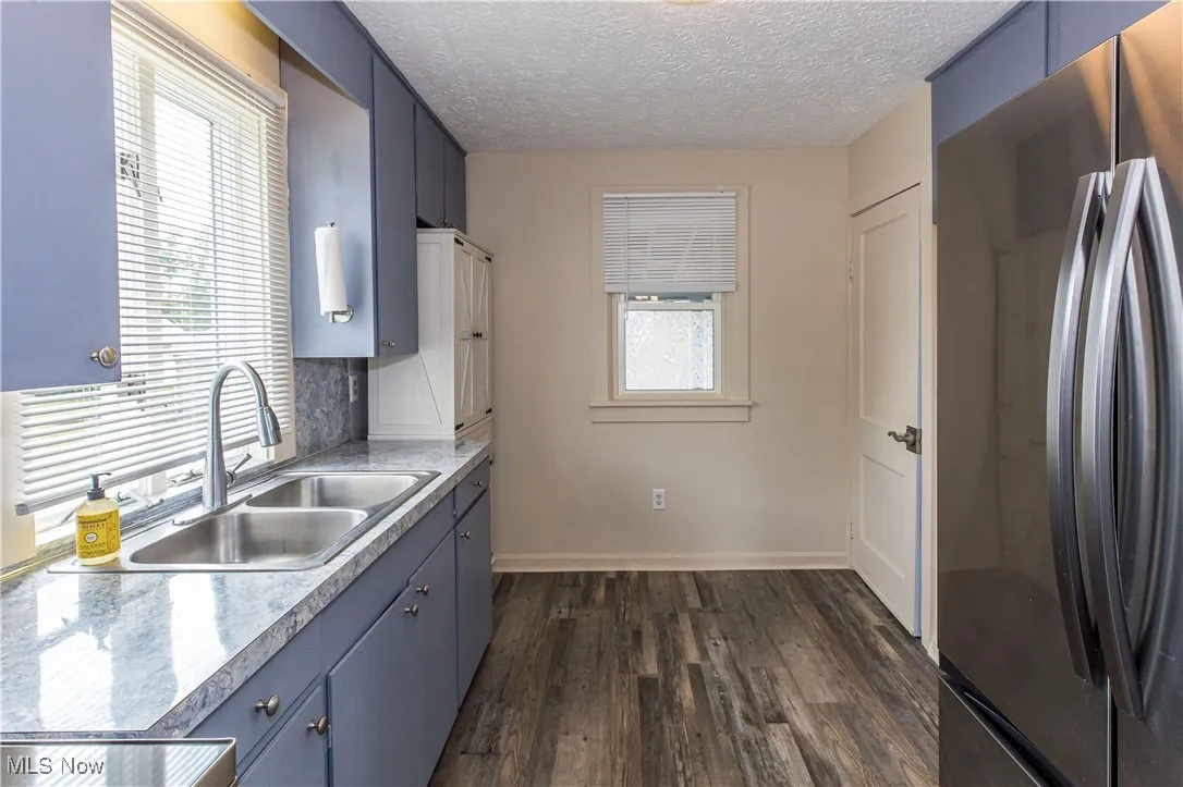 Kitchen with freestanding refrigerator, dark wood-style floors, blue cabinetry, light countertops, and a textured ceiling