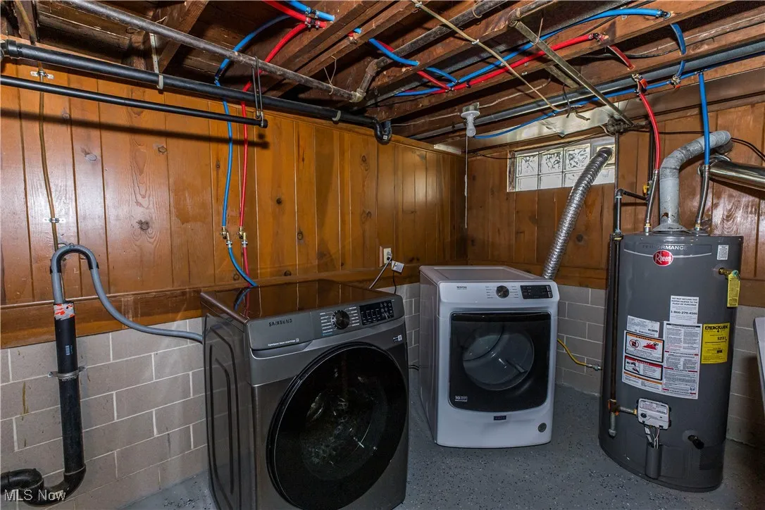 Laundry area featuring washing machine and clothes dryer, gas water heater, wood walls, and concrete block wall