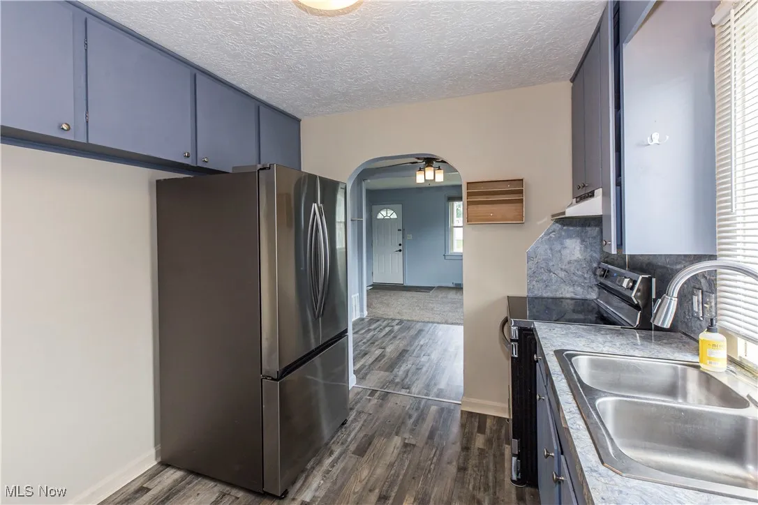 Kitchen featuring stainless steel appliances, arched walkways, dark wood finished floors, under cabinet range hood, and blue cabinetry