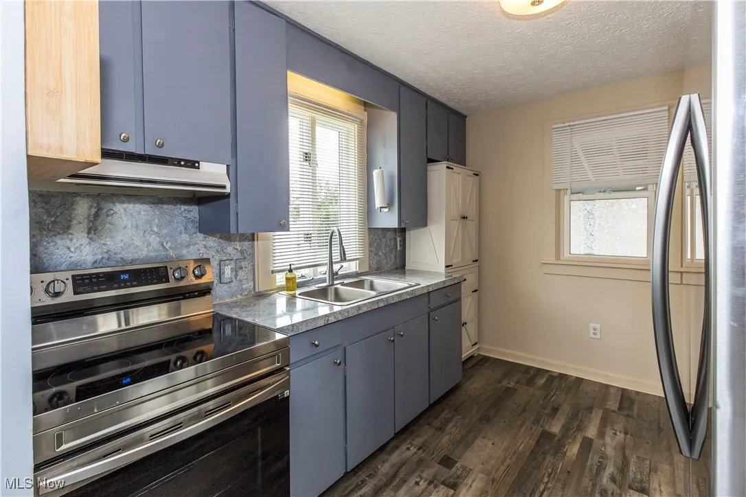 Kitchen featuring stainless steel appliances, backsplash, dark wood finished floors, under cabinet range hood, and a textured ceiling