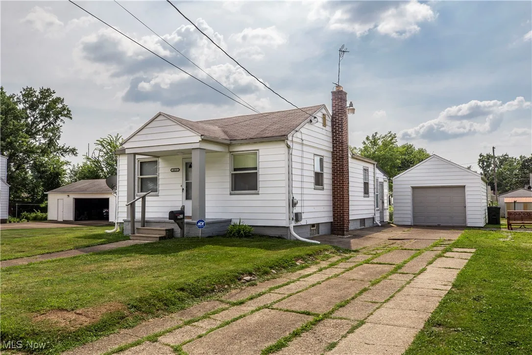 View of front of house with an outbuilding, a chimney, a detached garage, and a front yard