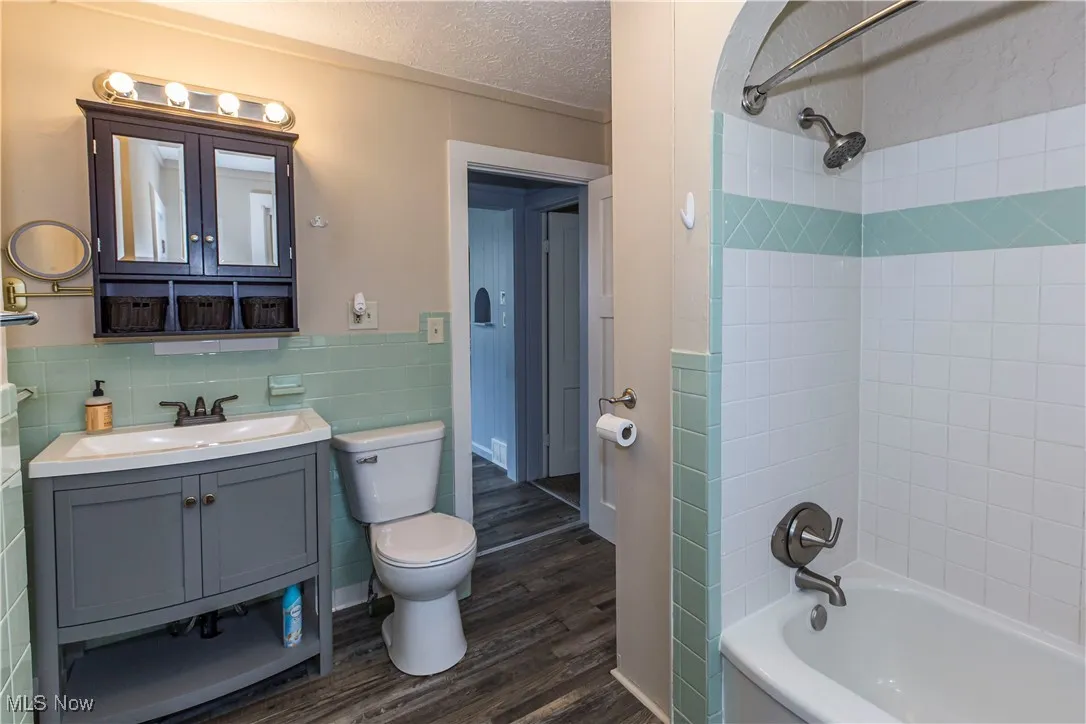 Full bath with tile walls, wood finished floors, vanity, shower / bathtub combination, and a textured ceiling