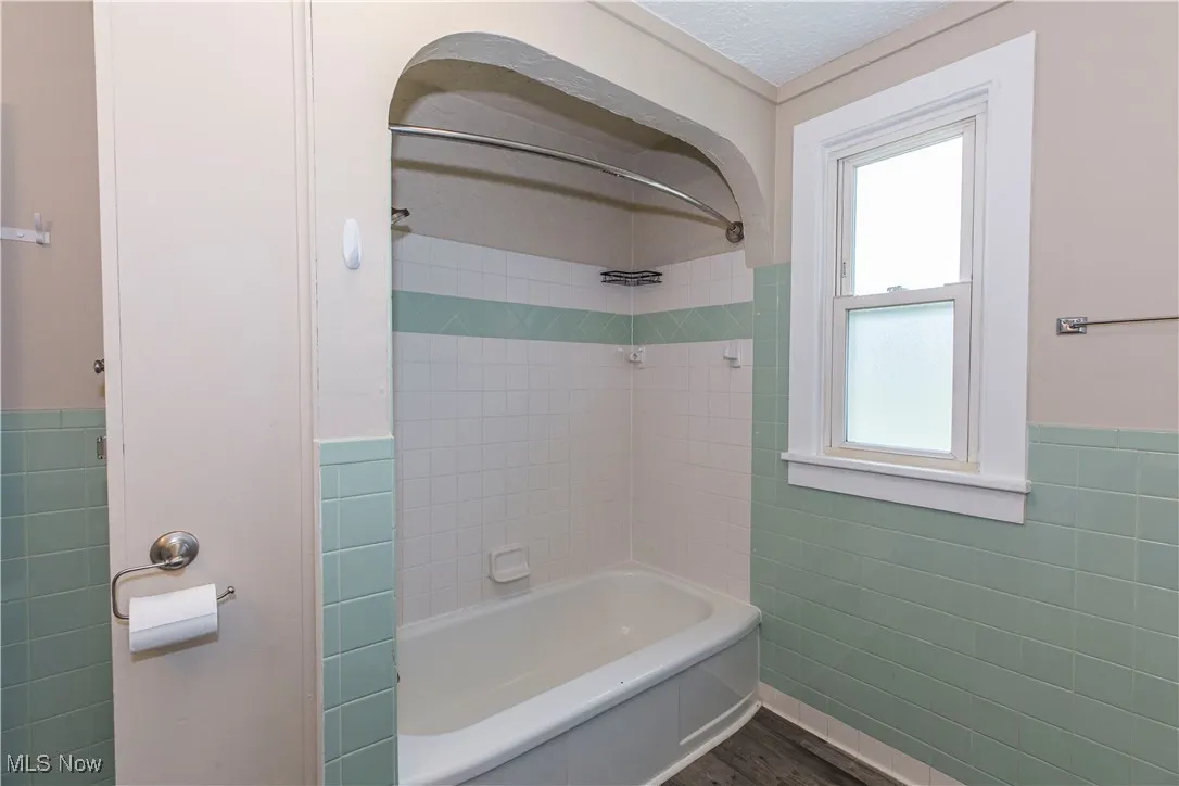 Full bathroom featuring tile walls, wainscoting, bathtub / shower combination, and wood finished floors