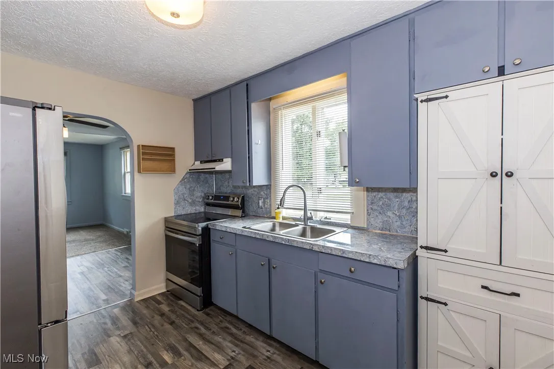 Kitchen with stainless steel appliances, arched walkways, dark wood-type flooring, backsplash, and under cabinet range hood