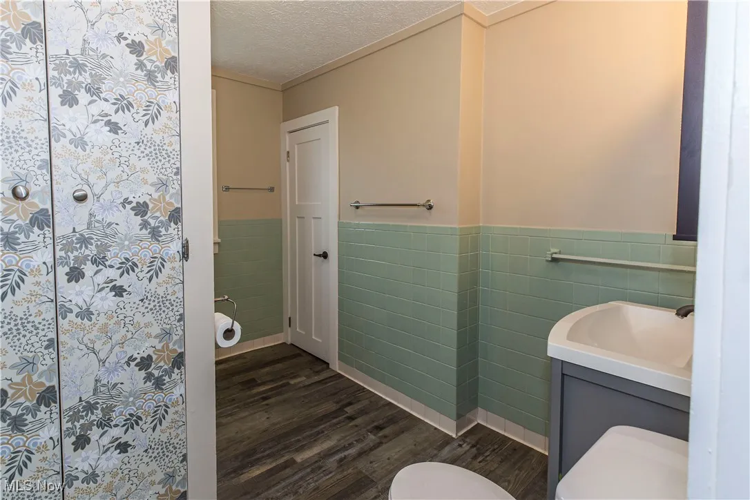 Full bath featuring tile walls, wood finished floors, wainscoting, vanity, and a textured ceiling