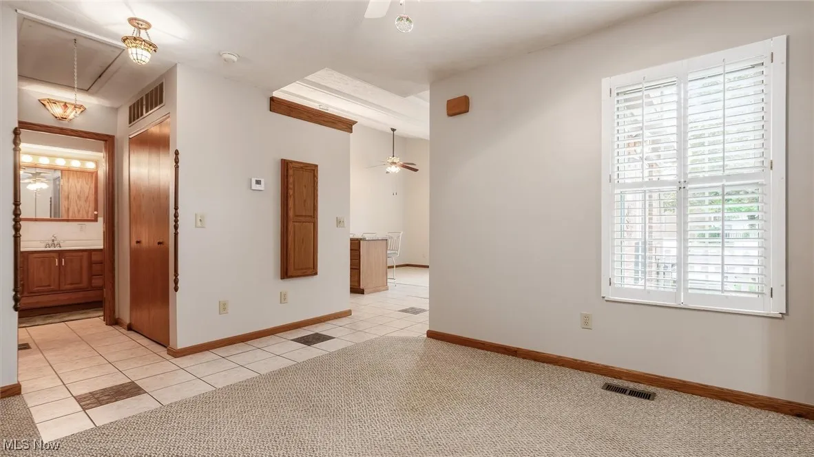 Spare room featuring ceiling fan, light tile patterned floors, and light carpet