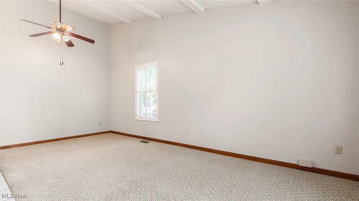 Empty room with a ceiling fan, light colored carpet, and beam ceiling