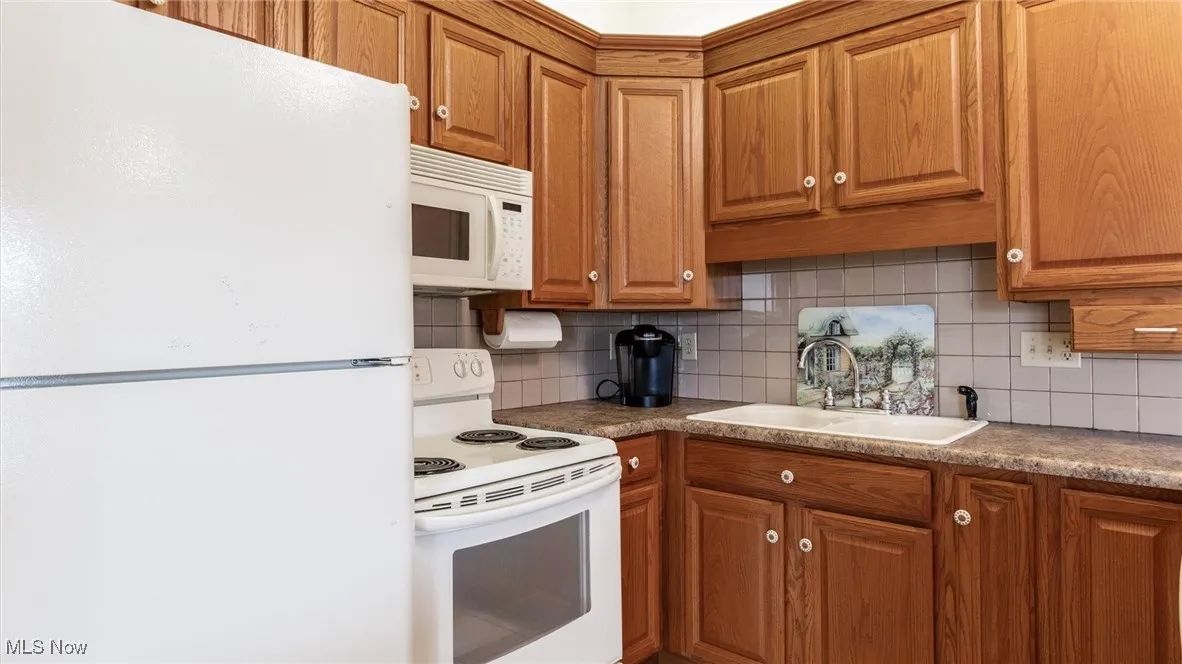 Kitchen with white appliances, tasteful backsplash, and brown cabinetry
