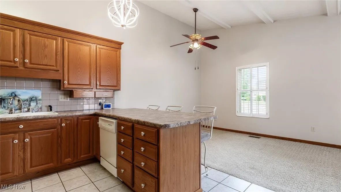 Kitchen with a peninsula, a kitchen breakfast bar, beamed ceiling, light carpet, and brown cabinetry
