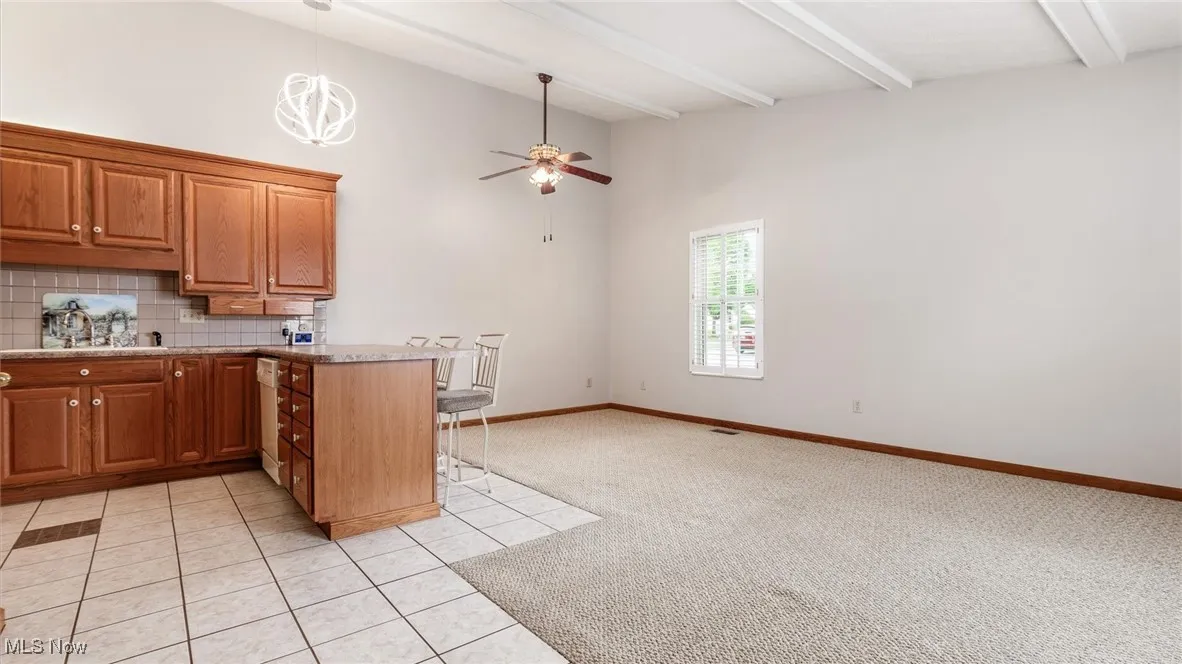 Kitchen featuring backsplash, a peninsula, a breakfast bar, beam ceiling, and ceiling fan