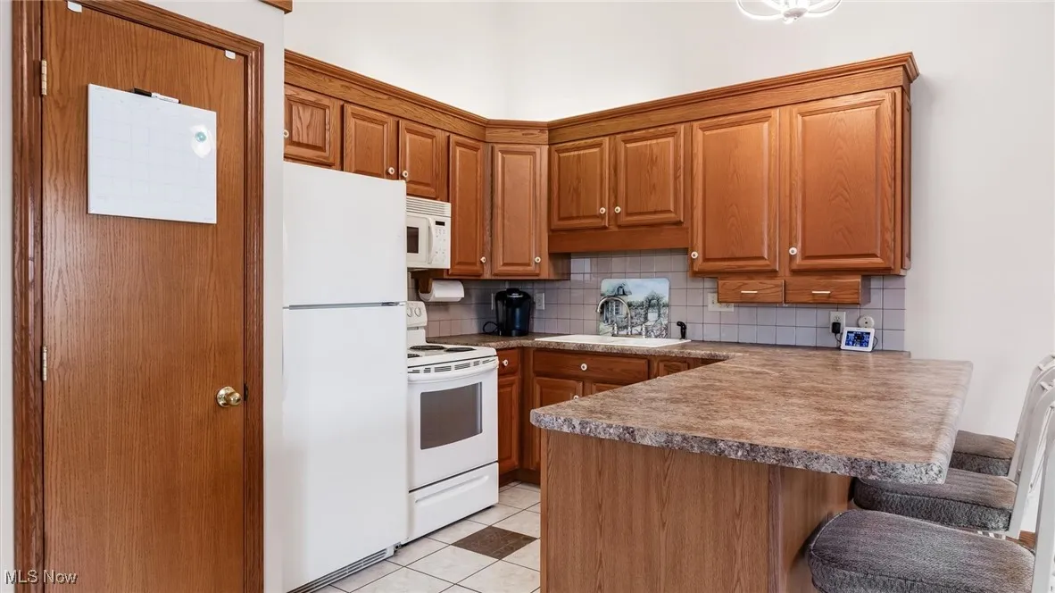 Kitchen featuring white appliances, a peninsula, decorative backsplash, and a breakfast bar area