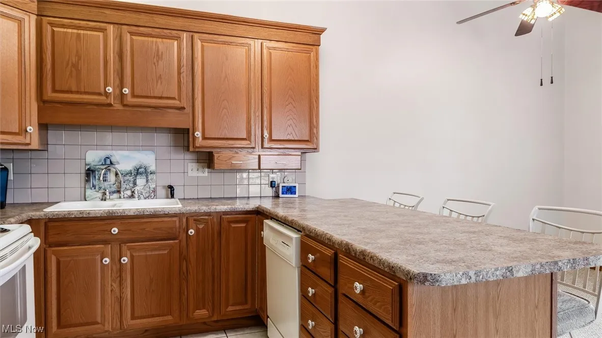 Kitchen with a peninsula, decorative backsplash, a ceiling fan, and brown cabinets