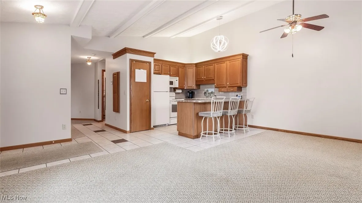 Kitchen featuring white appliances, a peninsula, a ceiling fan, decorative backsplash, and a kitchen breakfast bar
