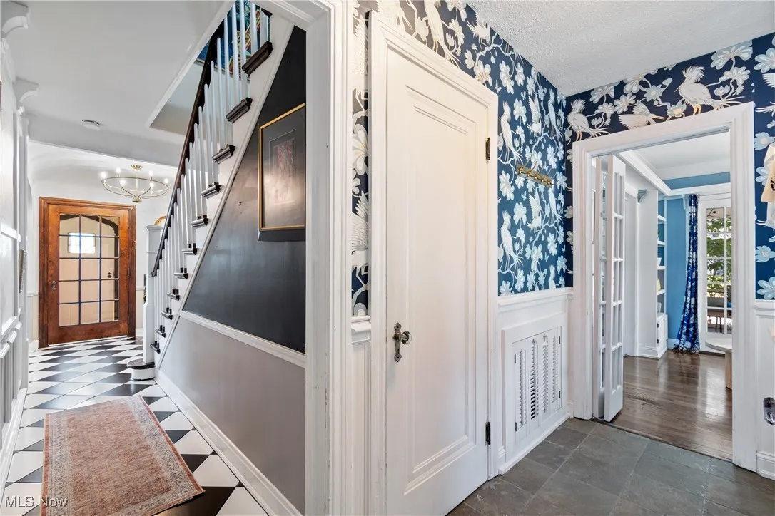 Corridor with wallpapered walls, stairway, wainscoting, and a chandelier