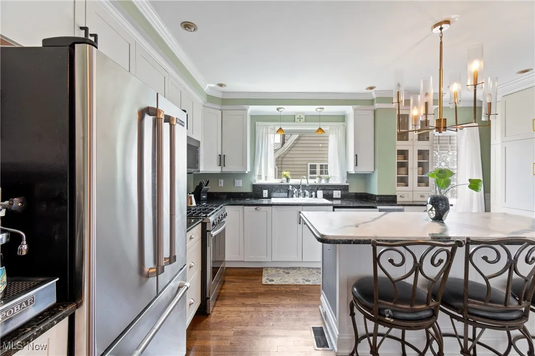 Kitchen with stainless steel appliances, ornamental molding, a chandelier, dark wood-style floors, and dark stone countertops