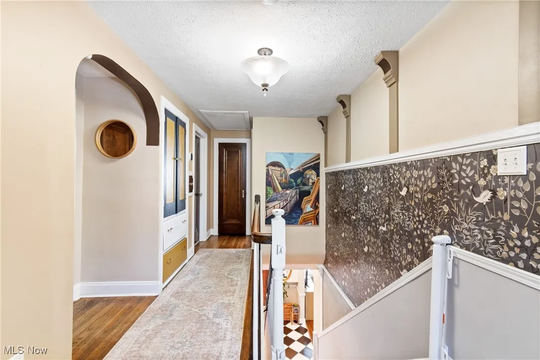 Hallway with a textured ceiling, wood finished floors, and arched walkways