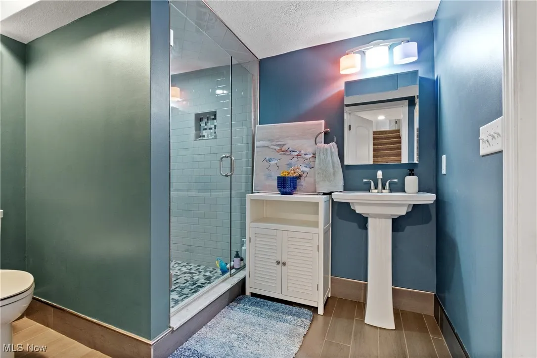 Bathroom featuring a shower stall, wood finish floors, and a textured ceiling