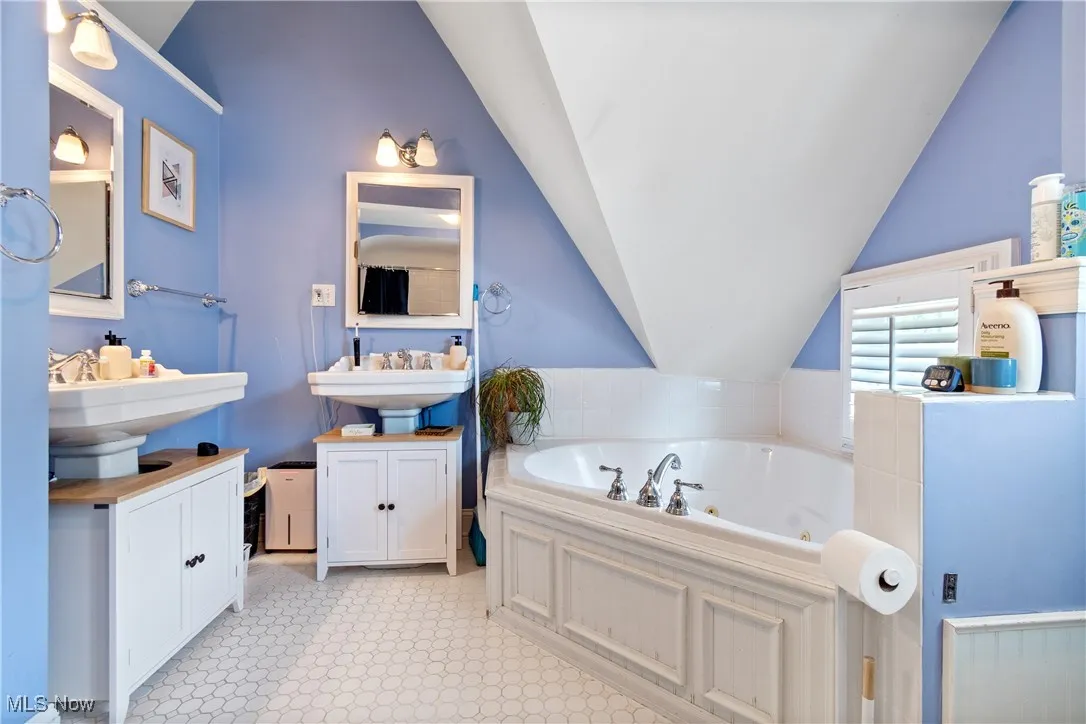 Bathroom featuring vaulted ceiling, two sinks, and a jetted tub