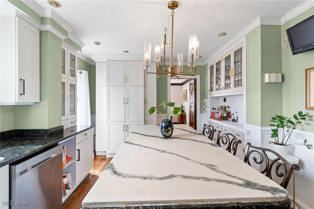 Kitchen with dishwasher, white cabinets, dark wood finished floors, and ornamental molding