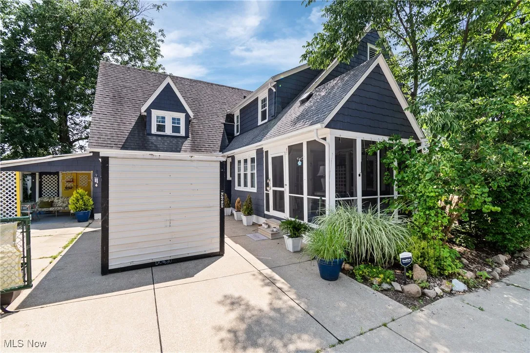 View of front facade featuring a sunroom, roof with shingles, and a patio
