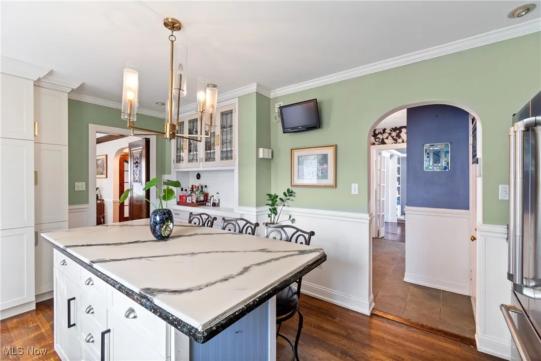 Kitchen featuring arched walkways, a center island, a wainscoted wall, white cabinets, and crown molding