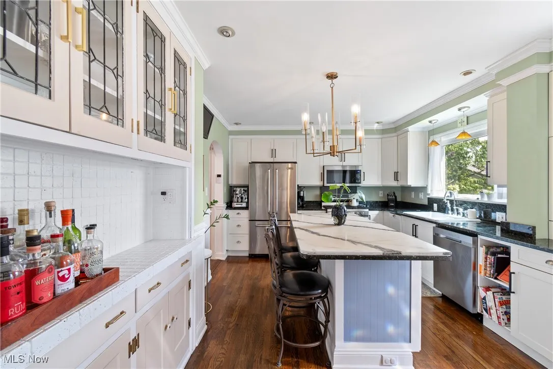 Kitchen featuring ornamental molding, appliances with stainless steel finishes, light stone counters, a chandelier, and decorative backsplash