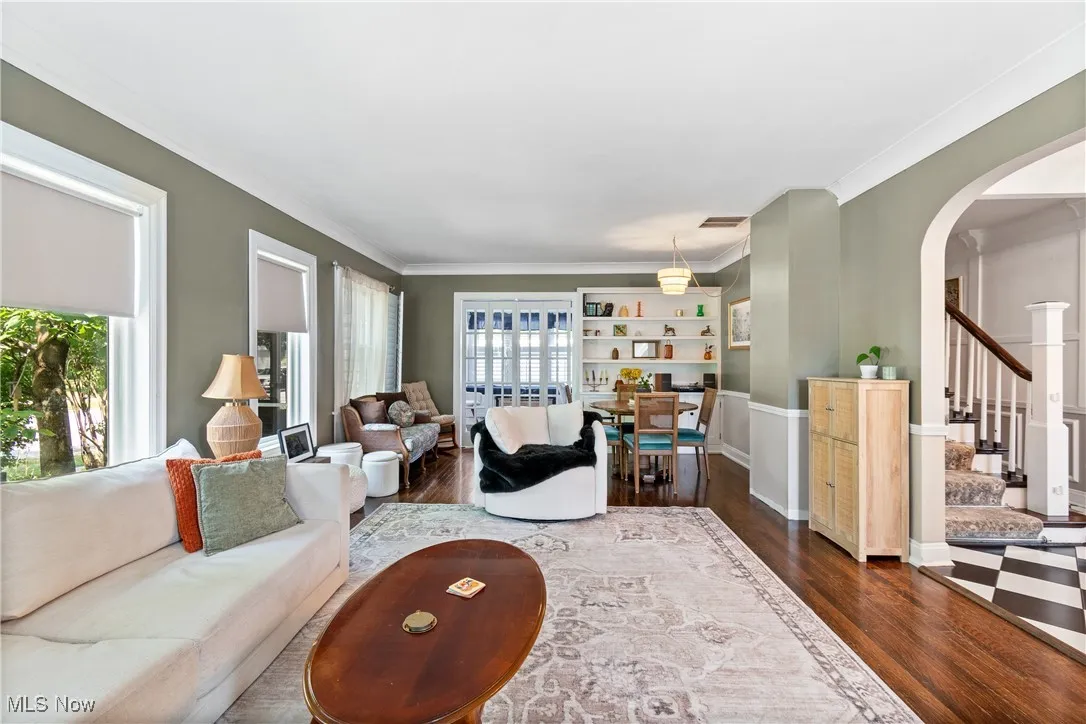 Living room featuring arched walkways, dark wood-style floors, ornamental molding, and stairs
