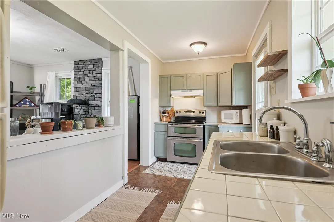 Kitchen featuring tile countertops, stainless steel appliances, open shelves, ornamental molding, and dark wood-style floors