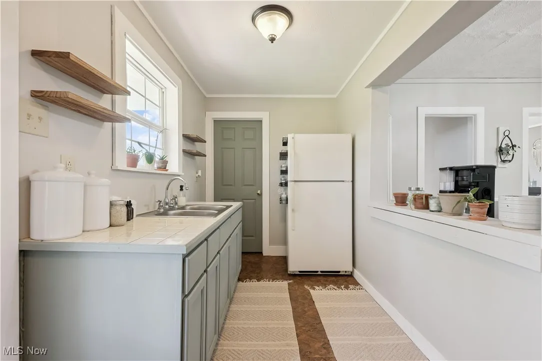 Kitchen featuring open shelves, freestanding refrigerator, ornamental molding, and gray cabinets