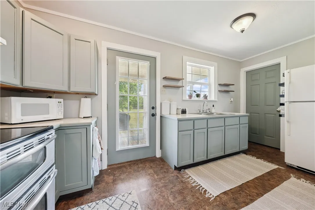 Kitchen featuring white appliances, open shelves, ornamental molding, light countertops, and gray cabinets