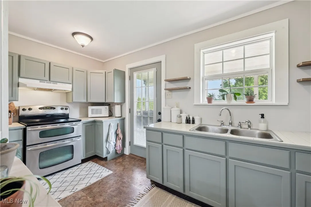 Kitchen featuring double oven range, under cabinet range hood, light countertops, open shelves, and white microwave