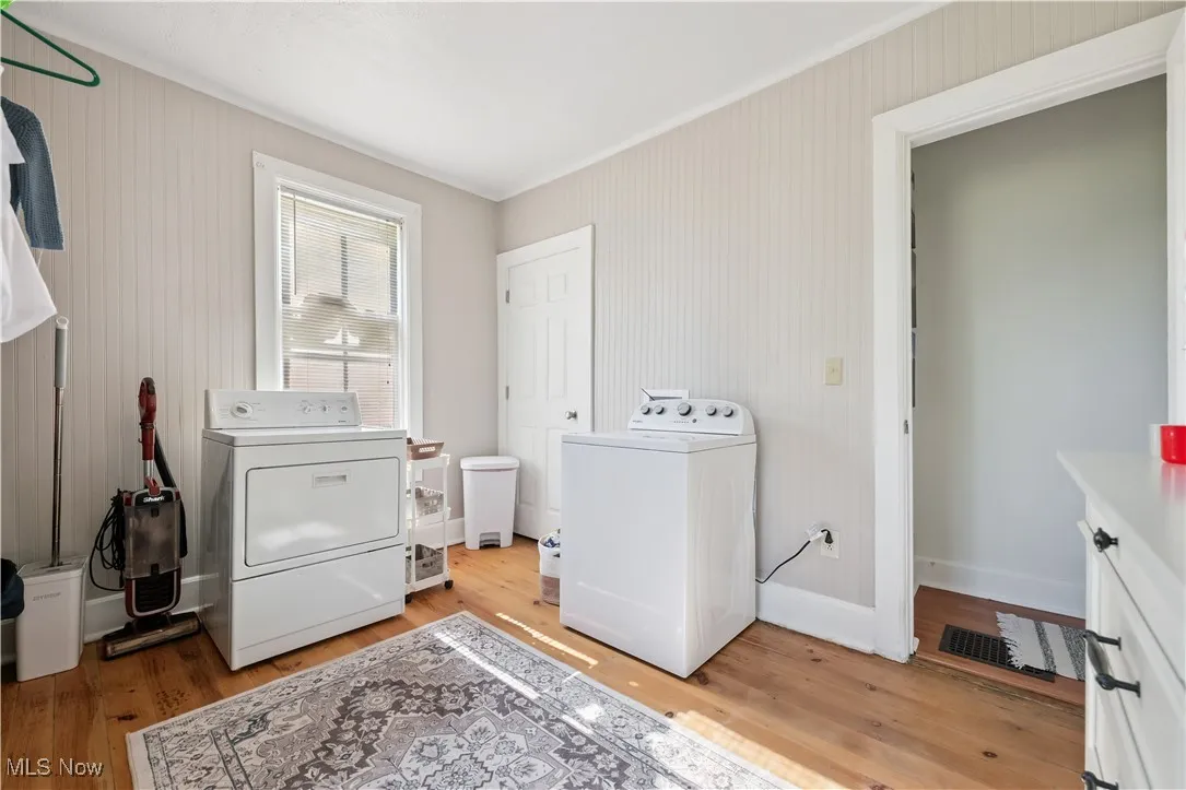 Laundry area featuring separate washer and dryer, light wood-type flooring, and crown molding