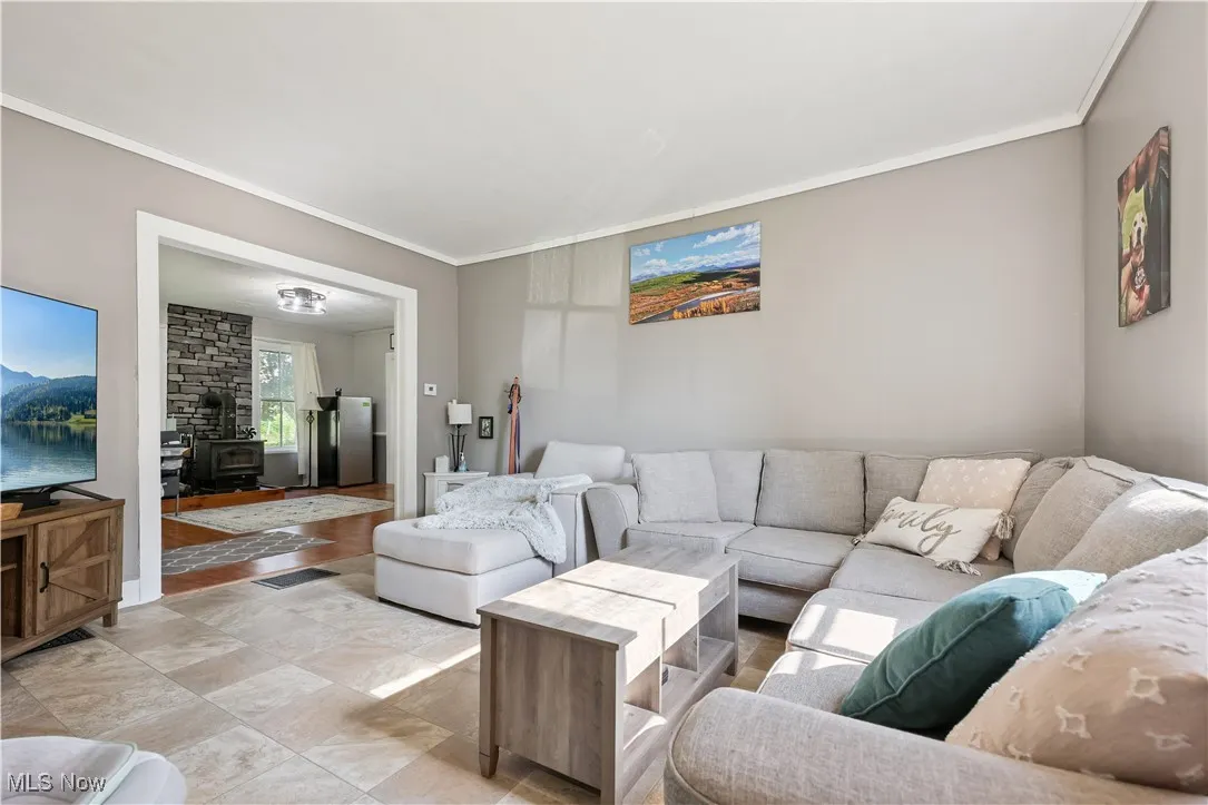 Living area with a wood stove, crown molding, and light flooring