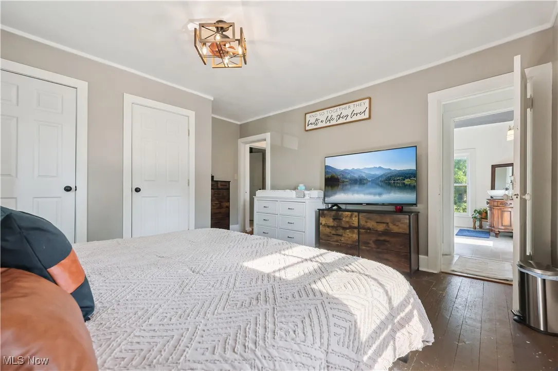 Bedroom with dark wood-type flooring, crown molding, and a chandelier