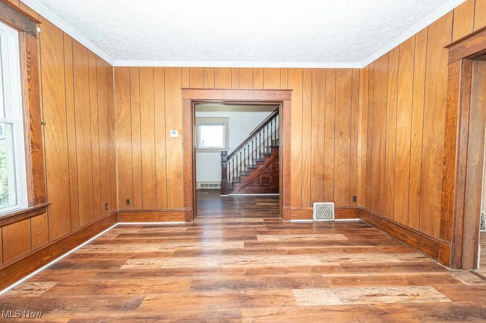 Living room with wood finished floors, wooden walls, a textured ceiling, stairway, and ornamental molding