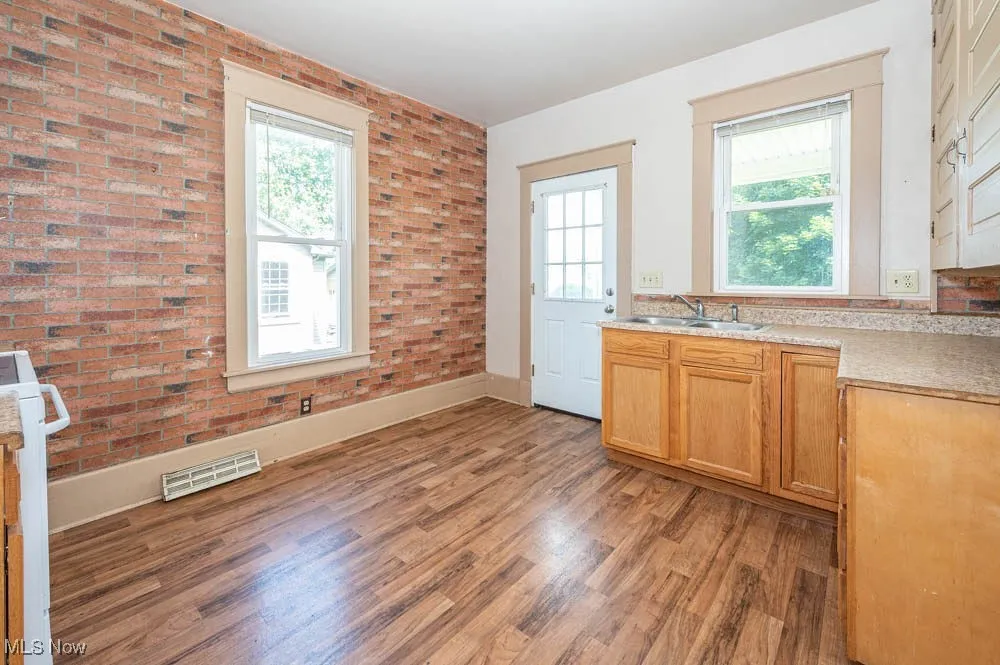 Kitchen with plenty of natural light, light wood-type flooring, light countertops, and brick wall