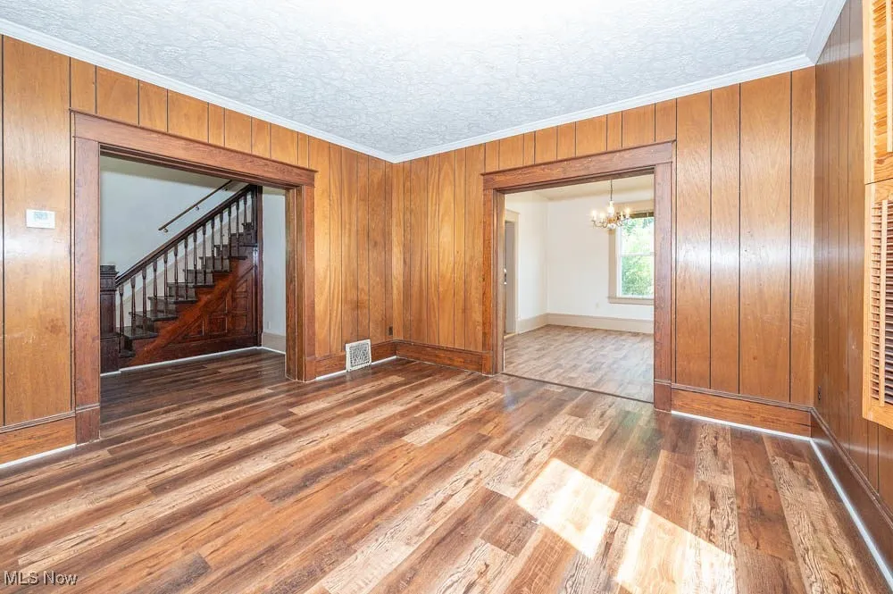 Unfurnished room with a chandelier, wood finished floors, stairway, ornamental molding, and wooden walls