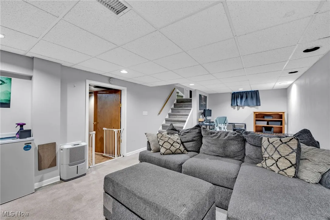 Carpeted living area with a paneled ceiling, stairs, and recessed lighting