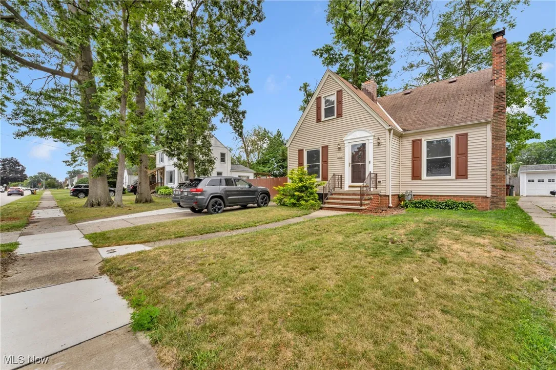 View of front facade with a chimney, a front lawn, concrete driveway, and roof with shingles