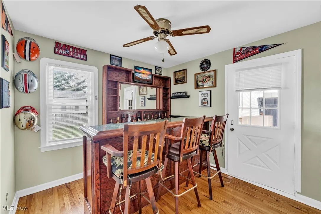 Indoor dry bar with ceiling fan, plenty of natural light, and wood finished floors