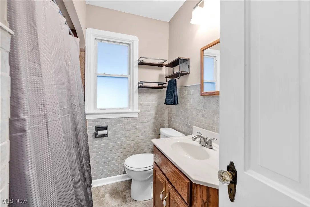 Bathroom featuring tile walls, vanity, wainscoting, curtained shower, and tile patterned flooring