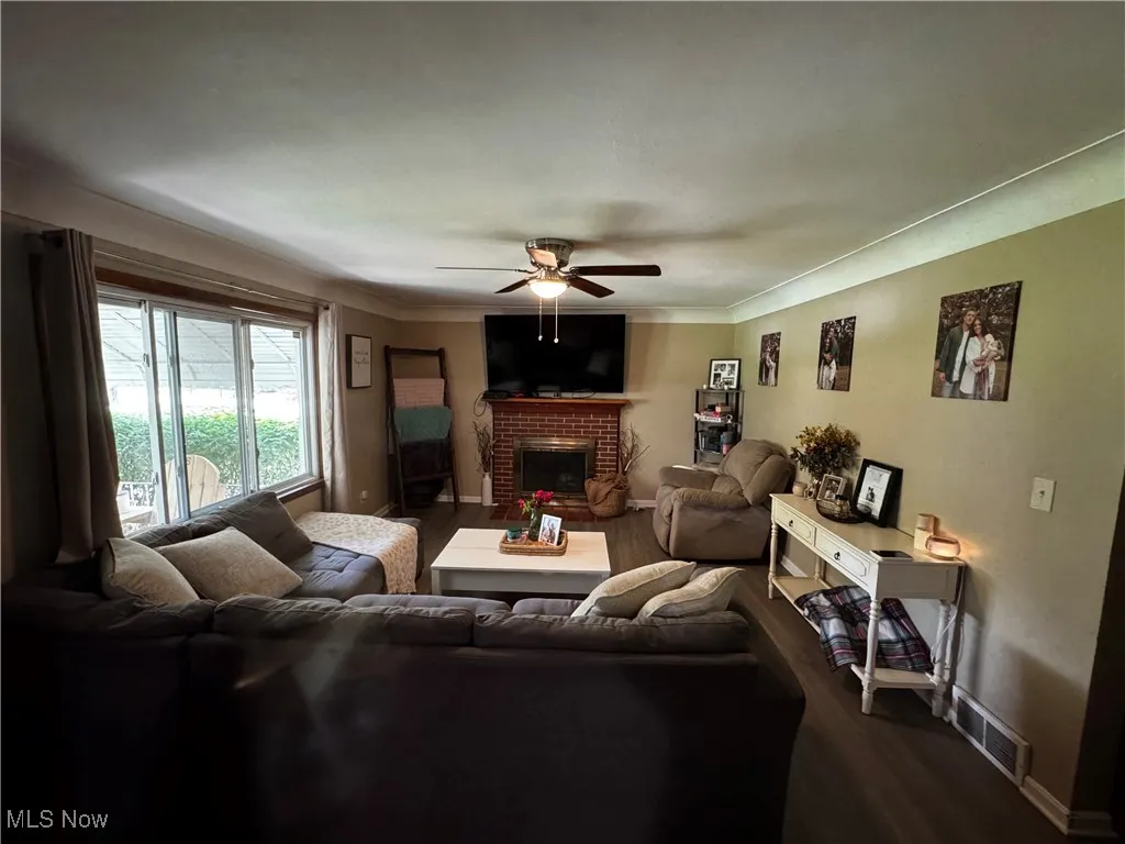 Living area featuring a ceiling fan, a fireplace, dark wood-type flooring, and crown molding