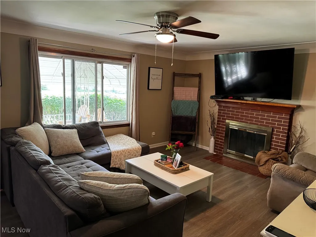 Living room with ceiling fan, dark wood-style floors, and a fireplace