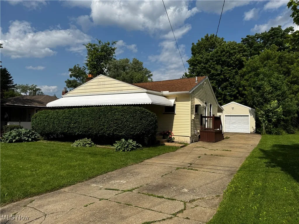 View of side of home with an outbuilding, a yard, a detached garage, and concrete driveway