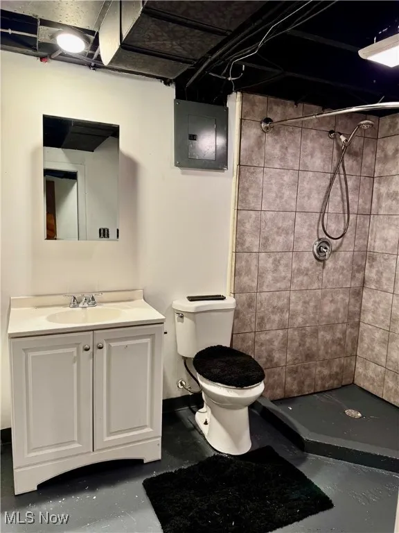 Bathroom with tiled shower, vanity, electric panel, and concrete floors