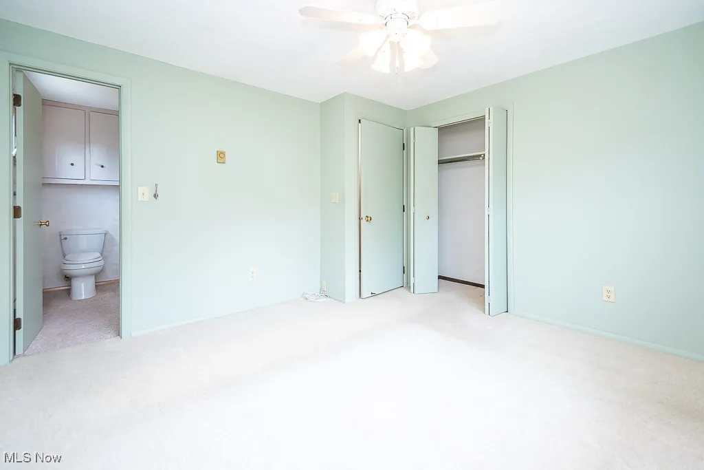 Unfurnished bedroom with light colored carpet, a closet, a ceiling fan, and connected bathroom