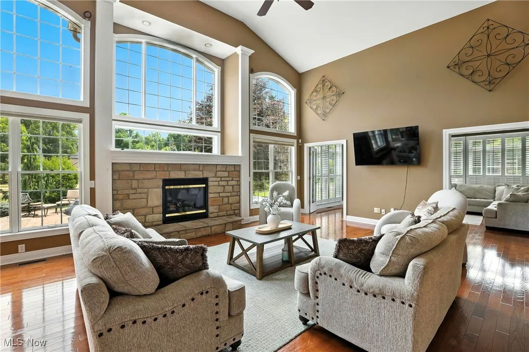 Living area with high vaulted ceiling, ceiling fan, wood-type flooring, and a fireplace